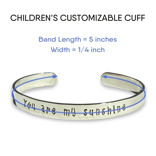 The Children’s Customizable Cuff Bracelet is silver with “You are my sunshine” engraved, a slightly open end, and measures 5" x 1/4". Blue lines and arrows show dimensions. Add your custom text above the engraving. Read more at Stamping Cat Studio (stampingcatstudio.com).
