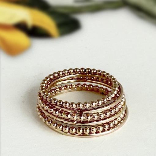 Five Stacking Boho And Midi Rings with a beaded texture are neatly stacked on a white surface, with a blurred green and yellow background that hints at out-of-focus leaves or flowers. Read more at Stamping Cat Studio (stampingcatstudio.com).