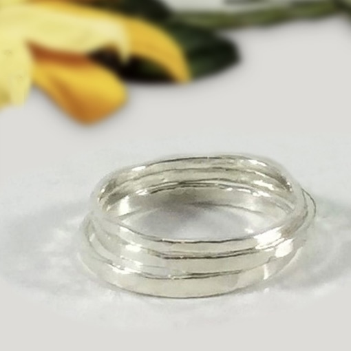 A close-up of the Stacking Boho And Midi Ring showcases its shiny silver interlocking bands. A softly blurred yellow flower with green leaves in the background highlights the elegance of this stackable accessory. Read more at Stamping Cat Studio (stampingcatstudio.com).