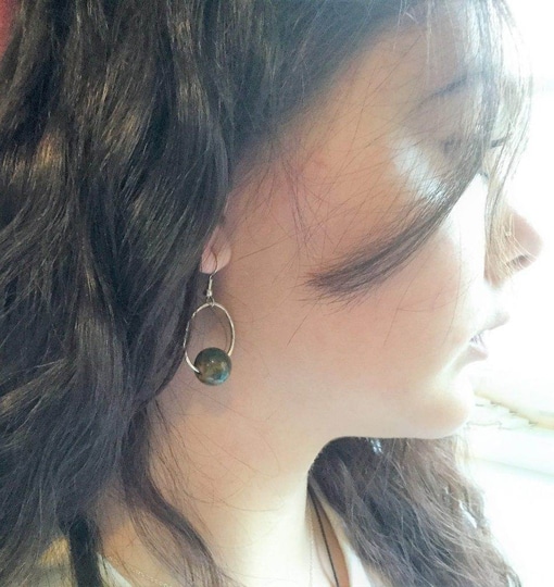 A woman with long, wavy dark hair is shown in profile facing right, wearing Natural Stone and Silver Hammered Earrings. Soft light highlights her cheek as strands of hair partially obscure her face. Read more at Stamping Cat Studio (stampingcatstudio.com).