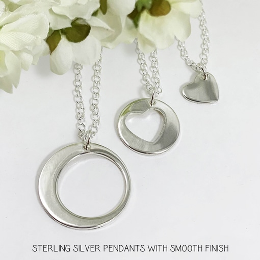 The Always Family Generations Necklace Set features three sterling silver pendants—a crescent moon, a circle with a cut-out heart, and a small heart—each shining with a smooth finish against delicate white flowers. Read more at Stamping Cat Studio (stampingcatstudio.com).