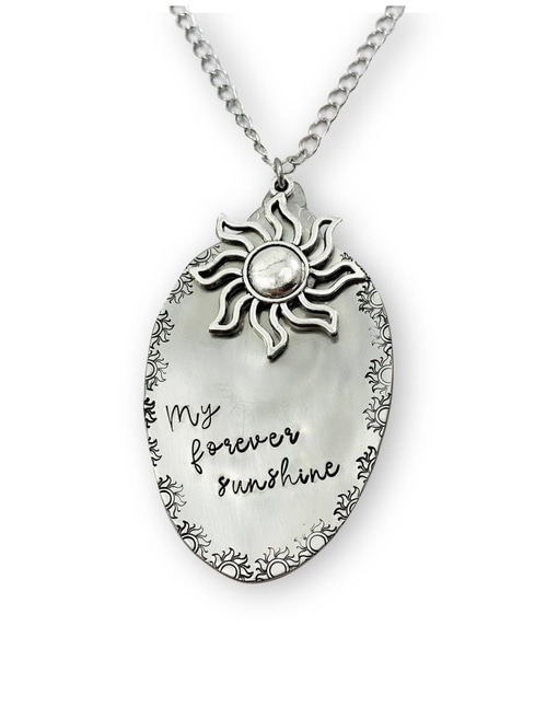 The Forever Sunshine Spoon Necklace features an oval silver pendant with a raised sun design, "My forever sunshine" handwritten-style engraving, ornate sun motif border, and hangs from a medium-length silver-toned chain. Read more at Stamping Cat Studio (stampingcatstudio.com).