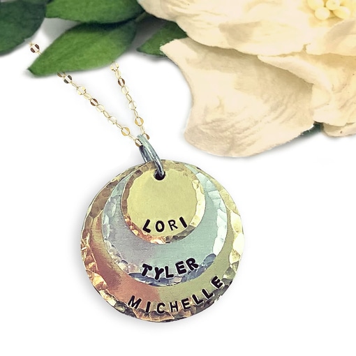 Kids Names Neck main new featuring three layered, hammered, circular metal charms stamped with the names “Lori,” “Tyler,” and “Michelle.” Read more at Stamping Cat Studio (stampingcatstudio.com).
