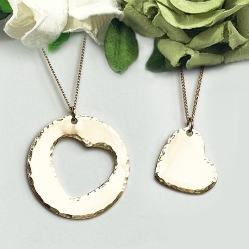 Couples Necklace main: Set of two gold necklaces—one with a large circle pendant and heart cutout, the other with a small heart pendant. Both have textured finishes and are displayed on white with green and white fabric flowers. Read more at Stamping Cat Studio (stampingcatstudio.com).
