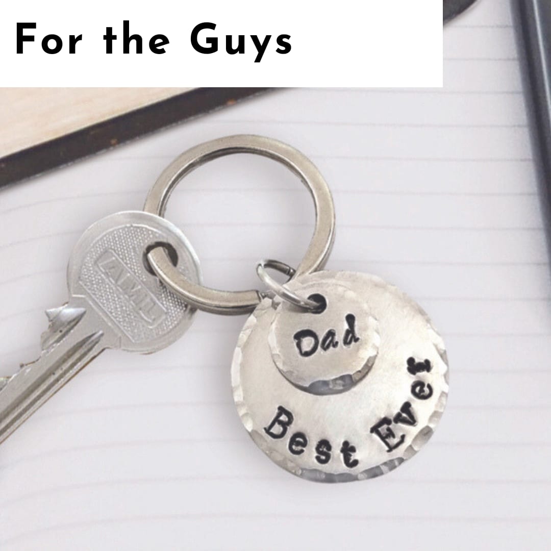 A metal keyring with a key and a round hammered metal tag engraved with “Dad” and “Best Ever” rests on a lined notebook, offering a thoughtful touch of personalized jewelry. The top of the image has text reading “For the Guys.”. Read more at Stamping Cat Studio (stampingcatstudio.com).